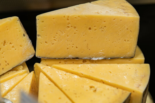 Close up of sliced yellow cheese with holes and wedge pieces. Dairy food ingredient for sandwich, appetizer, snack, cooking
