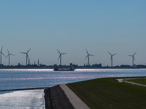 Aerial view of wind turbines at the Volkswagenwerk Emden industrial facility with a cargo ship sailing on the sparkling water in Emden, Niedersachsen, Germany.