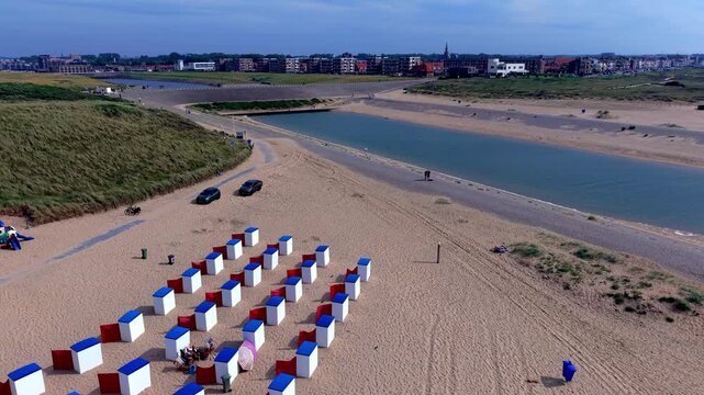 Aerial view video clip of Katwijk aan Zee beach resort, blue and white beach cabins, red windbreak screens, estuary canal, dunes, and town skyline in South Holland, Netherlands