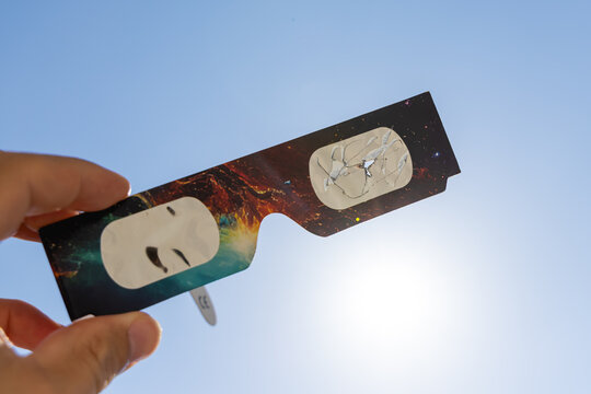 Gros plan sur une paire de lunettes d&rsquo;&eacute;clipse solaire avec des rayures, inutilisable et dangereux pour les yeux. En arri&egrave;re plan, le ciel bleu et le soleil.