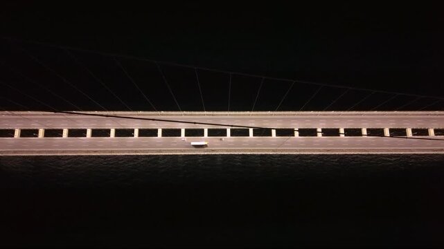 Top-down aerial night view of the illuminated 1915 &Ccedil;anakkale Bridge crossing the Dardanelles Strait in Turkey, showing the massive suspension bridge deck, empty highway lanes and dark sea below.