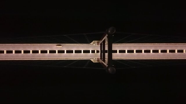 Top-down aerial night view of the illuminated 1915 &Ccedil;anakkale Bridge crossing the Dardanelles Strait in Turkey, showing the massive suspension bridge deck, empty highway lanes and dark sea below.
