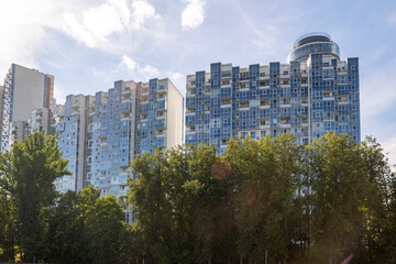 Fototapeta premium Moscow, Russia, August 5, 2026. High-rise blue glass residential buildings of the Mayak complex in Khimki behind green trees against a sunny sky with clouds.