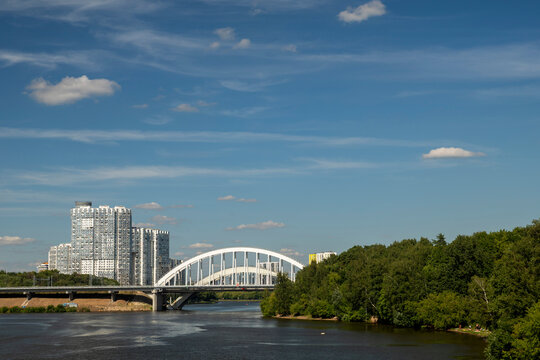 Moscow, Russia - August 5, 2026: Scenic view of the Khimki Railway Bridge spanning across the Moscow Canal, featuring modern high-rise residential buildings and lush green park zones under a blue sky.