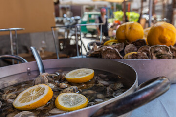 Pfanne mit Venusmuscheln und Zitronen in Palermo. Im Hintergrund eine Pfanne mit Austern und Zitronen. © laebema