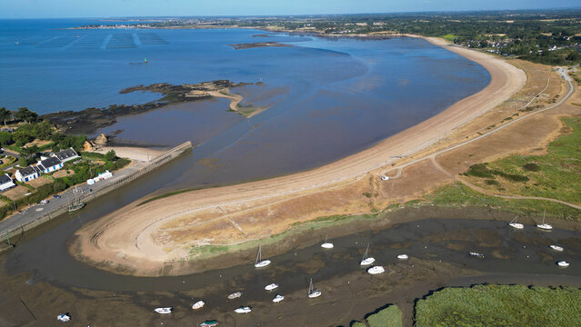 Aerial view of the coastal landscape in Billiers featuring a sandy beach, tidal flats with anchored boats, and lush greenery along the shoreline in Billiers, Brittany, France.
