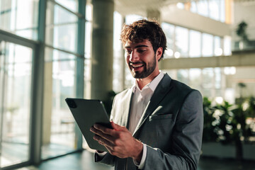 Fototapeta premium Professional businessman smiling while using tablet in modern office, embracing technology for work and communication