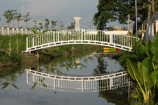 White Pedestrian Bridge Over Reflective Canal in Tropical Landscape