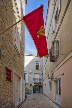 Historic red Venetian flag waving in Budva Old Town alley in Montenegro