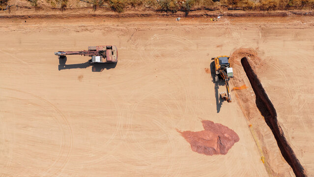Aerial view of two excavators working on a large dirt construction site with a deep trench and tire tracks in the dry ground in Athens, Greece.