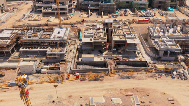 Aerial view of a large construction site featuring concrete building frames, steel rebar, yellow tower cranes, and temporary site offices in Athens, Greece.