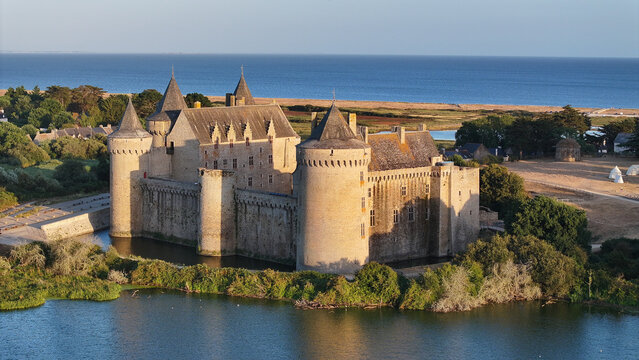 Aerial view of the historic Domaine de Suscinio castle surrounded by a moat and lush greenery near the coastline in Sarzeau, Bretagne, France.