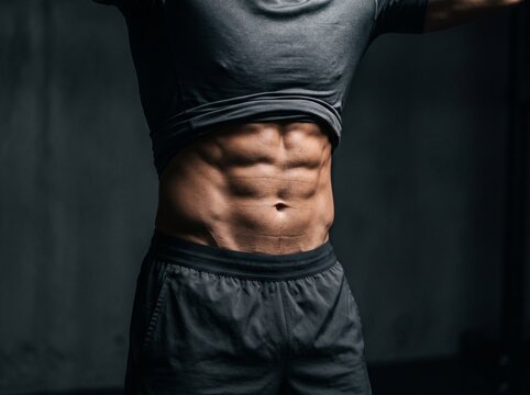 Close-up of fit athletic man showing muscular six pack abs in dark gym