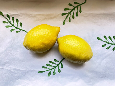 Leander, Texas, USA - July 6, 2026: Two fresh lemons resting on a simple green and white tablecloth with a leaf design.