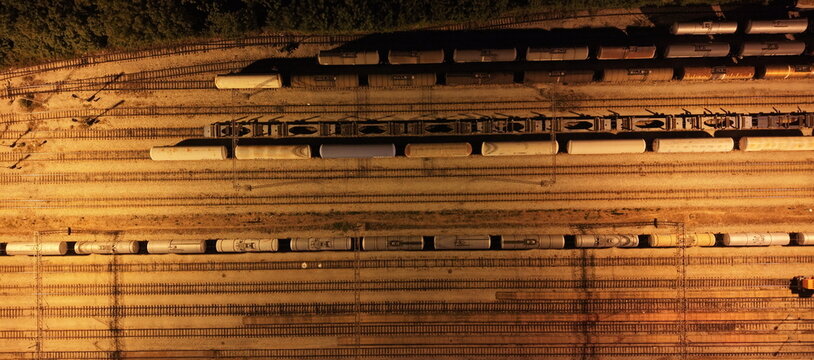 Aerial view of a freight train yard with multiple parallel tracks and rows of cargo cars illuminated by warm evening light in Omoljica, Vojvodina, Serbia.