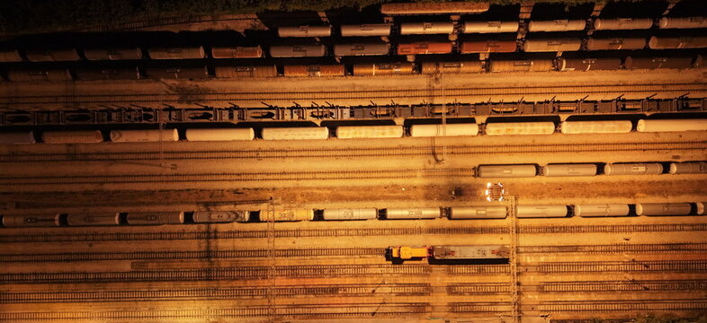 Aerial view of a railway yard at night with numerous freight train cars parked on parallel tracks illuminated by artificial lighting in Omoljica, Vojvodina, Serbia.