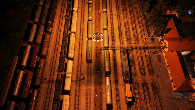 Aerial view of a train yard at night with multiple freight train cars parked on parallel tracks illuminated by bright overhead lights in Omoljica, Vojvodina, Serbia.