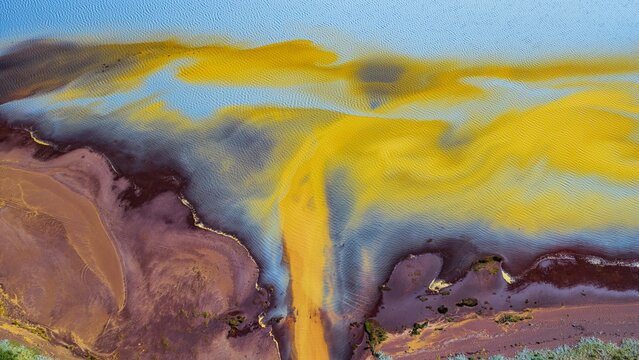 Aerial view of the Thjorsarver glacial river delta, showcasing vibrant yellow sediment patterns contrasting with deep blue water and dark brown riverbanks in Iceland.