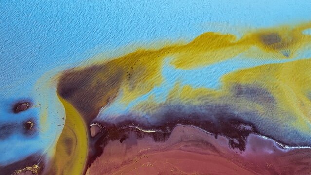 Aerial view of Thjorsarver glacial river patterns with vibrant yellow sediment and dark brown earth in Iceland.