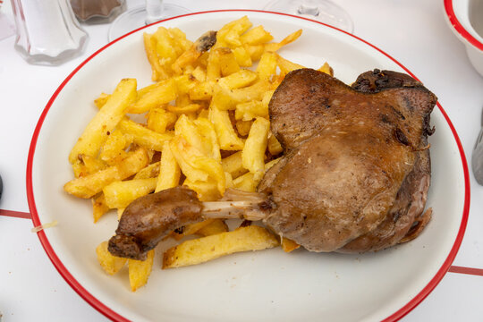 Perfectly cooked duck leg confit de canard with crispy golden skin and tender meat, served with golden French fries at authentic Parisian caf&eacute; bistro, paired with a glass of wine