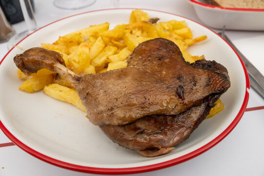 Perfectly cooked duck leg confit de canard with crispy golden skin and tender meat, served with golden French fries at authentic Parisian caf&eacute; bistro, paired with a glass of wine