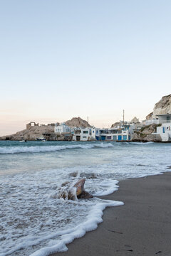 Vertical view of sunset at Firopotamos beach on Milos island, Greece, with a traditional whitewashed houses and church along the coast.