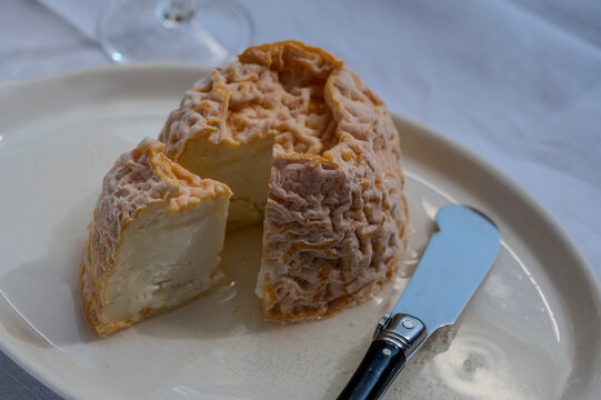 Small, round Langres cheese with orange washed rind and creamy center on a board, spooned and paired with Champagne