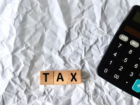 Wooden blocks forming the word TAX placed next to the corner of a black digital calculator on a white crumpled paper surface.