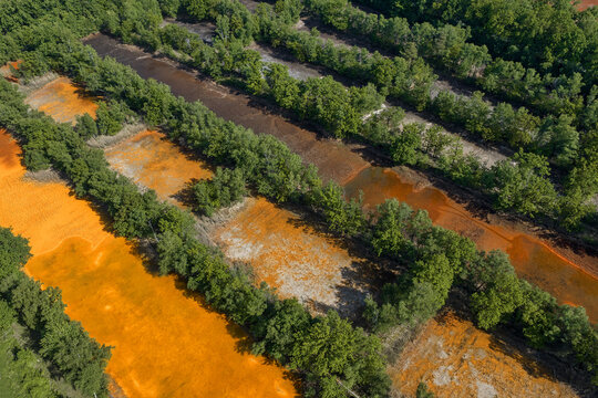 Aerial view of iron-rich orange water pools surrounded by dense green forest in Ibbenburen, North Rhine-Westphalia, Germany.