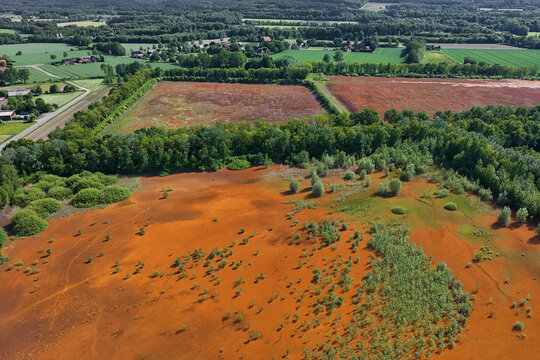 Aerial view of the unique orange-colored landscape with sparse vegetation, surrounding green forests, and agricultural fields in the distance, Ibbenburen, North Rhine-Westphalia, Germany.