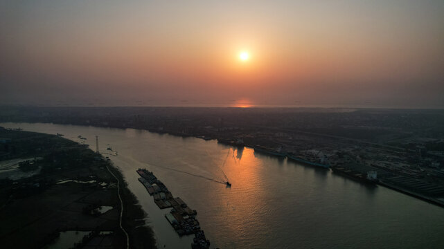 Aerial view of the Karnaphuli River at sunset with cargo ships and barges navigating the waterway in Chattogram, Chittagong Division, Bangladesh.