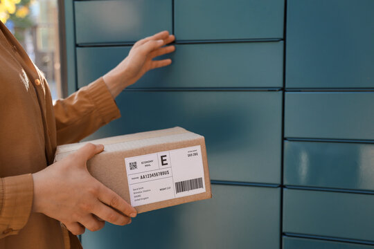 Person holding a cardboard package with a shipping label, preparing to place it into a parcel locker for delivery
