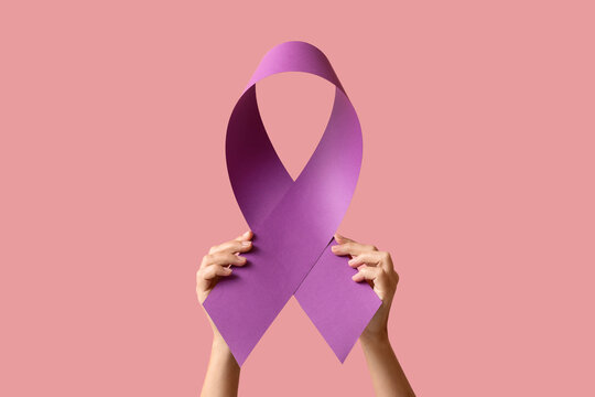 Hands holding a purple awareness ribbon, a symbol of support for various causes, on a pink background