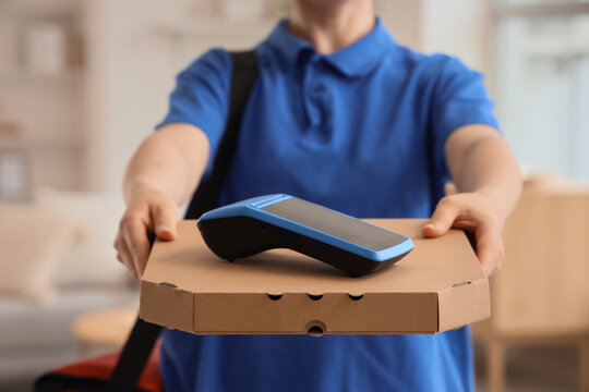 Delivery person in blue uniform holding a pizza box with a payment terminal for contactless transactions