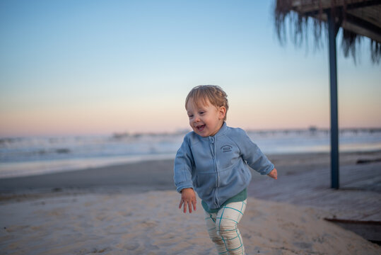 A 20-month-old toddler boy running happily along the beach during autumn, wearing a warm jacket and pants in the cool weather