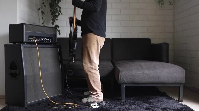 A front view shot of a man sitting down to practice on his electric bass at home