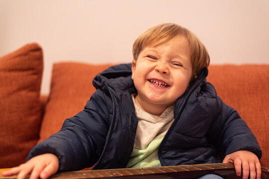 A smiling 22-month-old toddler boy holding the neck of a guitar, with only part of the instrument visible in the frame