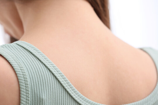 Womans bare neck and shoulder with a light green ribbed tank top, close up view of skin texture and clothing detail
