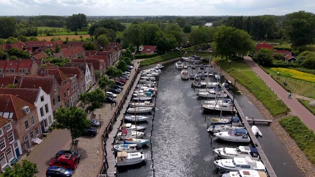 Aerial view video clip of Veere historic town harbor, canal with moored yachts and boats, car parking lot, traditional brick houses, and countryside in Zeeland, Netherlands