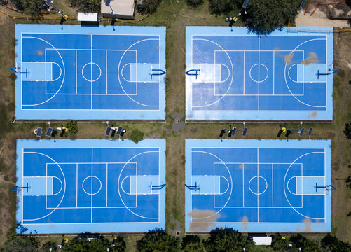 Aerial view of four vibrant blue multi-sport courts with white markings, surrounded by patches of grass and solar-powered lighting fixtures in San Luis Potosi, San Luis Potosi, Mexico.