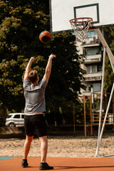 Basketball player practicing shooting skills on outdoor court in urban environment during bright daylight © Nikola Spasenoski