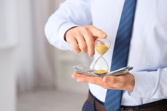 Businessman with hourglass and dollar banknotes in office