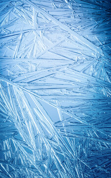 Ice frozen in intricate patterns of delicate crystals with brilliant contrasts of deep blues. Real unique patterned crystal formations. Sparkling window frost or icy cold winter frosting background.