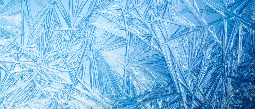 Ice frozen in intricate patterns of delicate crystals with brilliant contrasts of deep blues. Real unique patterned crystal formations. Sparkling window frost or icy cold winter frosting background.