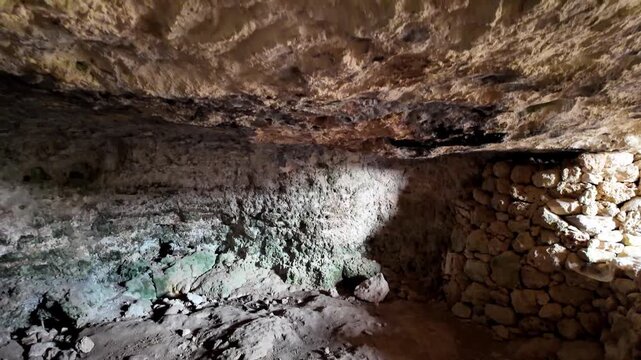 Malta, Xemxija Heritage trail, Punic caves. Dark cavern walls glow with green mineral streaks. Stone structures hint at ancient human habitation. Natural textures and earth tones evoke mystery and his