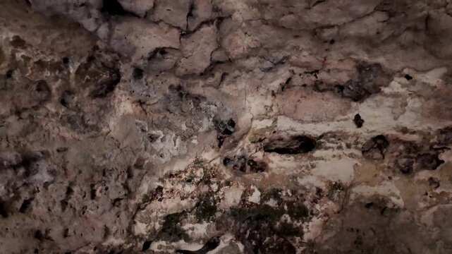 Malta, Xemxija Heritage trail, Punic caves celling and holes. Dark cave walls show rough, ancient stone textures. Moisture and moss cling to worn, crumbling surfaces. Narrow, shadowy opening invites e