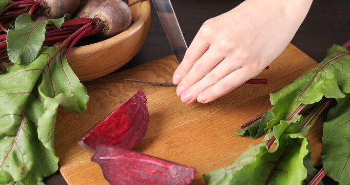 Woman cutting fresh young beet into halves at table, closeup