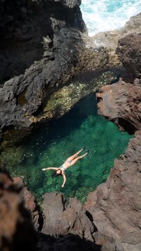 Woman floating in a natural volcanic rock pool on a sunny day