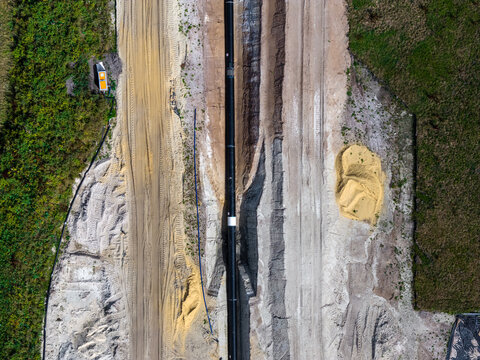 Aerial view of a pipeline running through the industrial grounds of ZE PAK S.A. Elektrownia Patnow, featuring sandy soil, tire tracks, and surrounding greenery in Konin, Wielkopolskie, Poland.