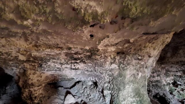 Dark cave walls reveal ancient, mossy textures. Natural rock formations show erosion over time. Light highlights crevices, emphasizing the cave's age and mystery